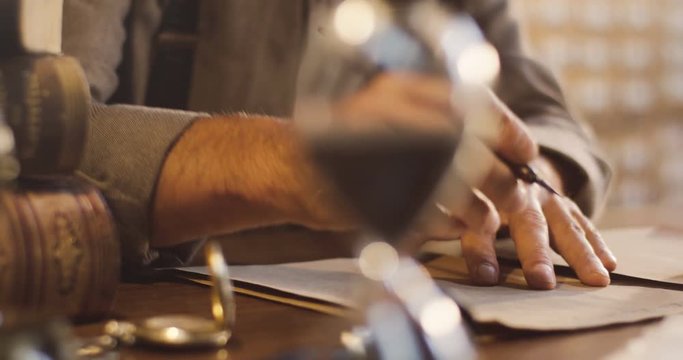 Close up of the old male hands wetting a pen in the ink and starting to write on the old wooden desk.
