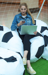 Girl with phone and laptop on the football field
