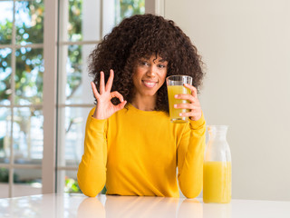 African american woman drinking healthy fruit juice at home doing ok sign with fingers, excellent symbol