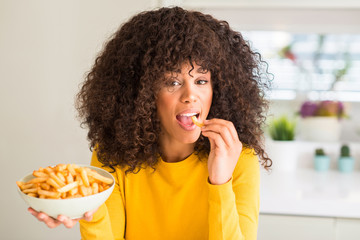 Fototapeta na wymiar African american woman holding a plate with potato chips at home with a confident expression on smart face thinking serious