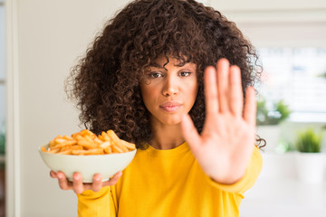 Fototapeta na wymiar African american woman holding a plate with potato chips at home with open hand doing stop sign with serious and confident expression, defense gesture