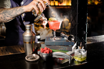 Bartender spraying on the red transperent cocktail standing on the books