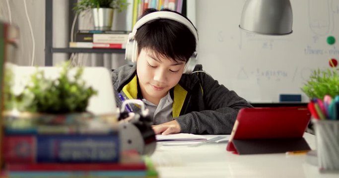 Young teenage student listen to music from tablet computer and doing homework at home, Dolly move left to right.