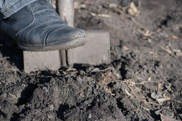 A fragment of a leg of the worker who digs with a shovel empty box with topsoil.