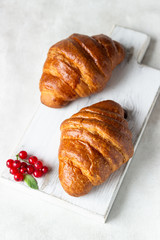Fresh croissants with red currant on a light grey background