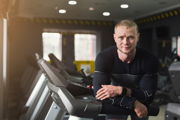 Young man having rest in gym after running on treadmill