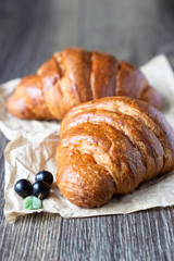 Fresh croissants with black currant on an old wooden background