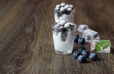 Ice cubes with berries and mint leaves  in glasses on wooden background