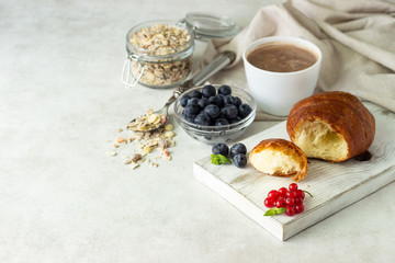 Croissant with fresh berries, muesli and a cup of coffee or hot chocolate on a light background. Copy space