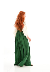 full length portrait of red haired girl wearing long green gown,. standing pose with back to the camera, isolated on white studio background.