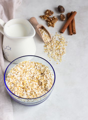 Multigrain cereal flakes in a blue glass bowl, jug of milk, spices (nutmeg and cinnamon) and walnuts. Ingredient for preparing healthy breakfast. Concept of healthy food. Copy space for text.