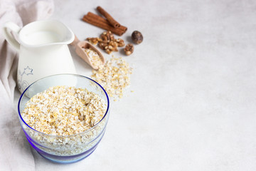 Multigrain cereal flakes in a blue glass bowl, jug of milk, spices (nutmeg and cinnamon) and walnuts. Ingredient for preparing healthy breakfast. Concept of healthy food. Copy space for text.