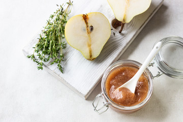 Pear jam, fresh pears and thyme on wooden board on light background.