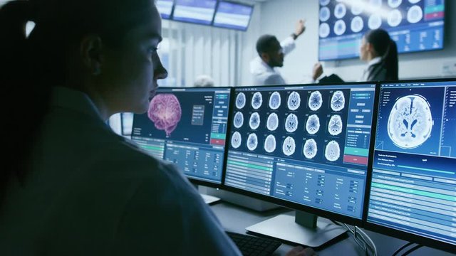 Over the Shoulder Shot of Female Medical Scientist Working with CT Brain Scan Images on a Personal Computer in Laboratory.  Shot on RED EPIC-W 8K Helium Cinema Camera.