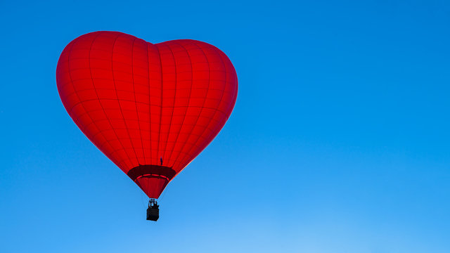 Bright red hot air balloon in the shape of heart against blue sk