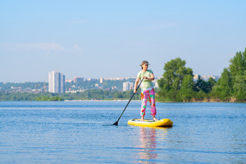 Woman sails on a SUP board on the cityscape background