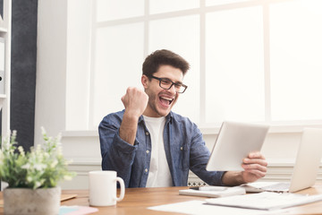 Young happy businessman in office with tablet
