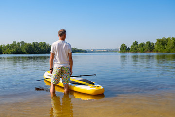 Man is standing next to SUP board on the beach