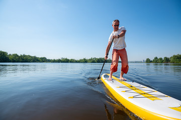 Joyful man in sunglasses sails on a SUP board in large river