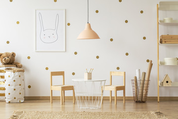 Pastel lamp above table between chairs in gold kid's room interior with poster. Real photo