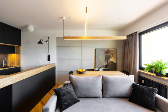 Pillows on grey sofa in modern apartment interior with black kitchen and light above table. Real photo
