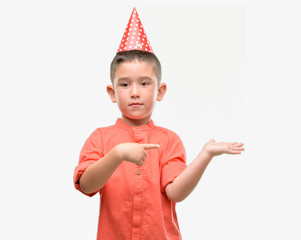 Dark haired little child wearing birthday cap very happy pointing with hand and finger