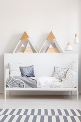 Triangles on white headboard above bed in teenager's bedroom interior with carpet. Real photo