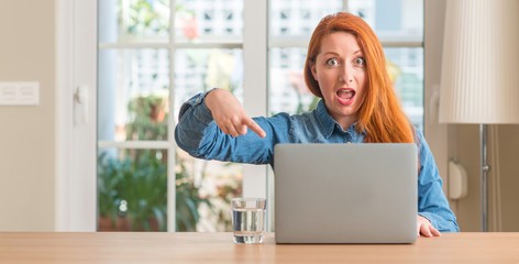 Redhead woman using computer laptop at home very happy pointing with hand and finger
