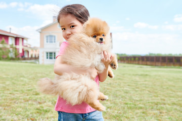 Waist up portrait of cute Asian girl posing with Pomeranian puppy standing in front yard of two storey house, copy space