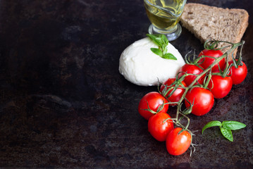 Fresh basil, mozzarella cheese, olive oil and cherry tomatoes on dark background. Italian food or ingredients background. Caprese. Copy space, top view.