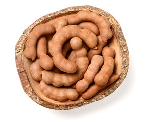 fresh tamarind fruits and leaves in the wooden bowl, isolated on the white background, top view