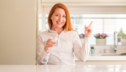 Thirsty redhead woman and glass of water very happy pointing with hand and finger to the side