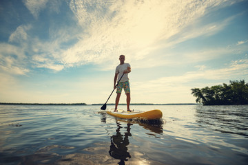 Joyful man is training  SUP board in large river