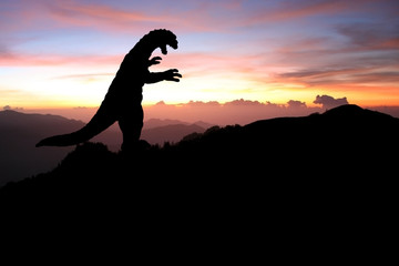 Silhouette eines Godzilla-artigen Monsters auf einem Berg bei Sonnenaufgang