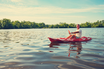Happy adult man kayaking on the river at a sunny morning