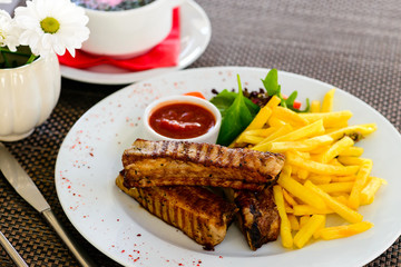 Juicy grilled meat with tasty French fries and sauce on the plat