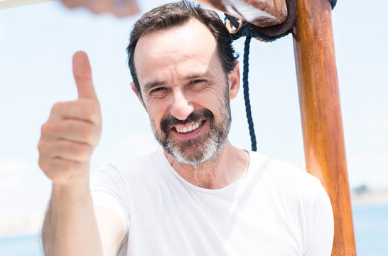 Handsome senior man traveling on sailboat happy with big smile doing ok sign, thumb up with fingers, excellent sign