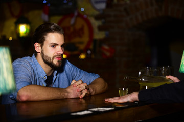 Man with beard sits at bar counter on pub background.