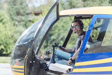 Pilot training. Upbeat young man sitting in a pilot booth of a helicopter and smiling at the camera, being ready to start his training
