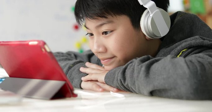 Dolly shoot of Young asian boy playing on tablet computer with headphone at home,