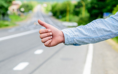 Fototapeta premium Most popular way of hitchhiking is to thumb up. Hand thumb up gesture try stop car road background. Thumb or hand gesture hitchhiking. Make sure you know right gestures used locally to stop car