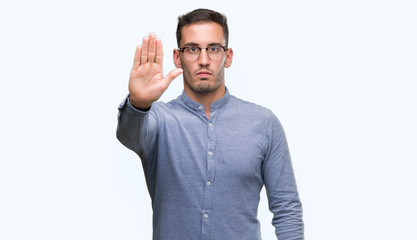 Fototapeta premium Handsome young elegant man wearing glasses doing stop sing with palm of the hand. Warning expression with negative and serious gesture on the face.