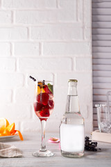 alcohol cocktail with fresh fruits and berries with a bottle of tonic and a place under the text on the bottle on white wooden background