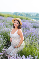 beautiful pregnant woman in white dress touching belly in violet lavender field