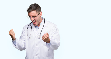 Handsome young doctor man very happy and excited doing winner gesture with arms raised, smiling and...
