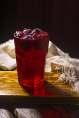 Frozen icy red berries in a glass on crumpled wrapping paper standing on a vintage wooden table.