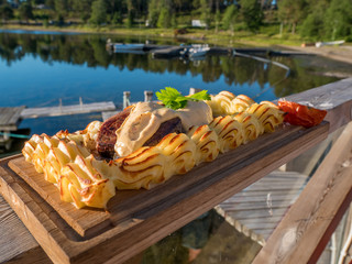 Meat steak on plank with mash potatoes puree on a wood board. Outside with lake in background. Swedish style plankstek.