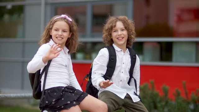 The children are waving their hands. A boy and a girl in school uniform greet their classmates. Back to school