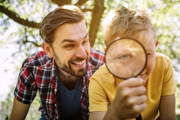 Fototapeta premium Portrait of child and father. Son is looking on camera through loop. Guy is laughing and looking on camera as well. They are enjoying spending time together.