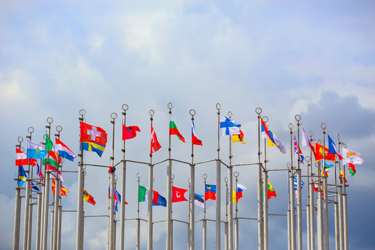 Flags of European states on flagpoles against blue sky background.